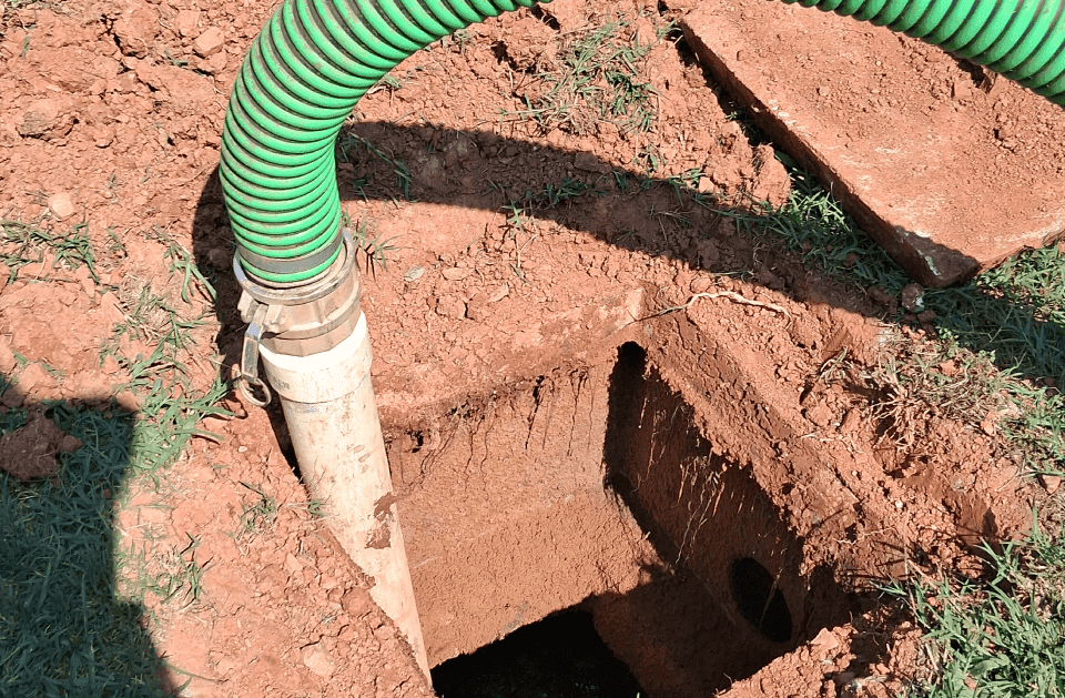 Green vacuum hose seated in an excavated septic tank opening during a pump-out