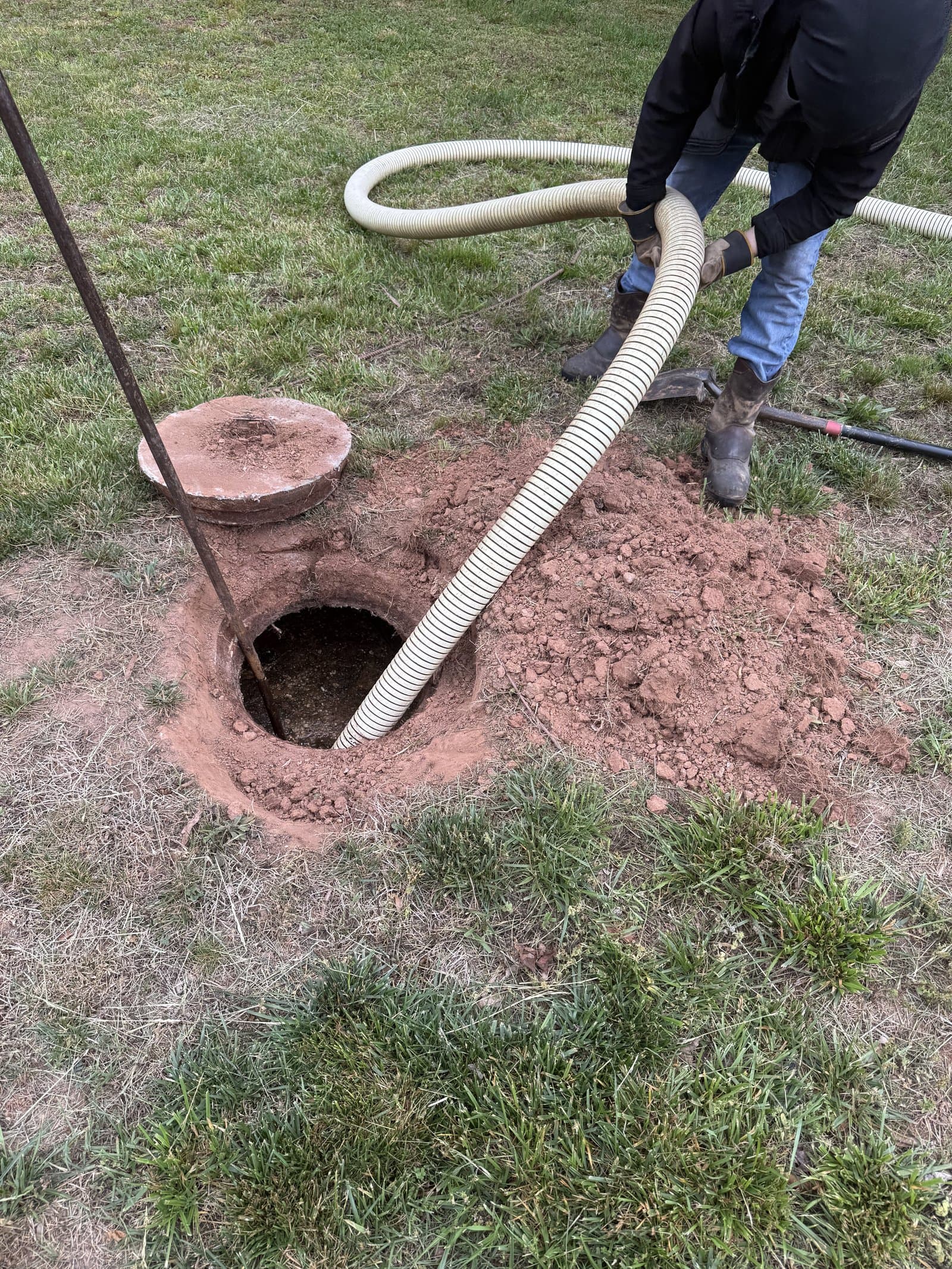 Technician in protective gloves positioning the vacuum hose over an open septic tank