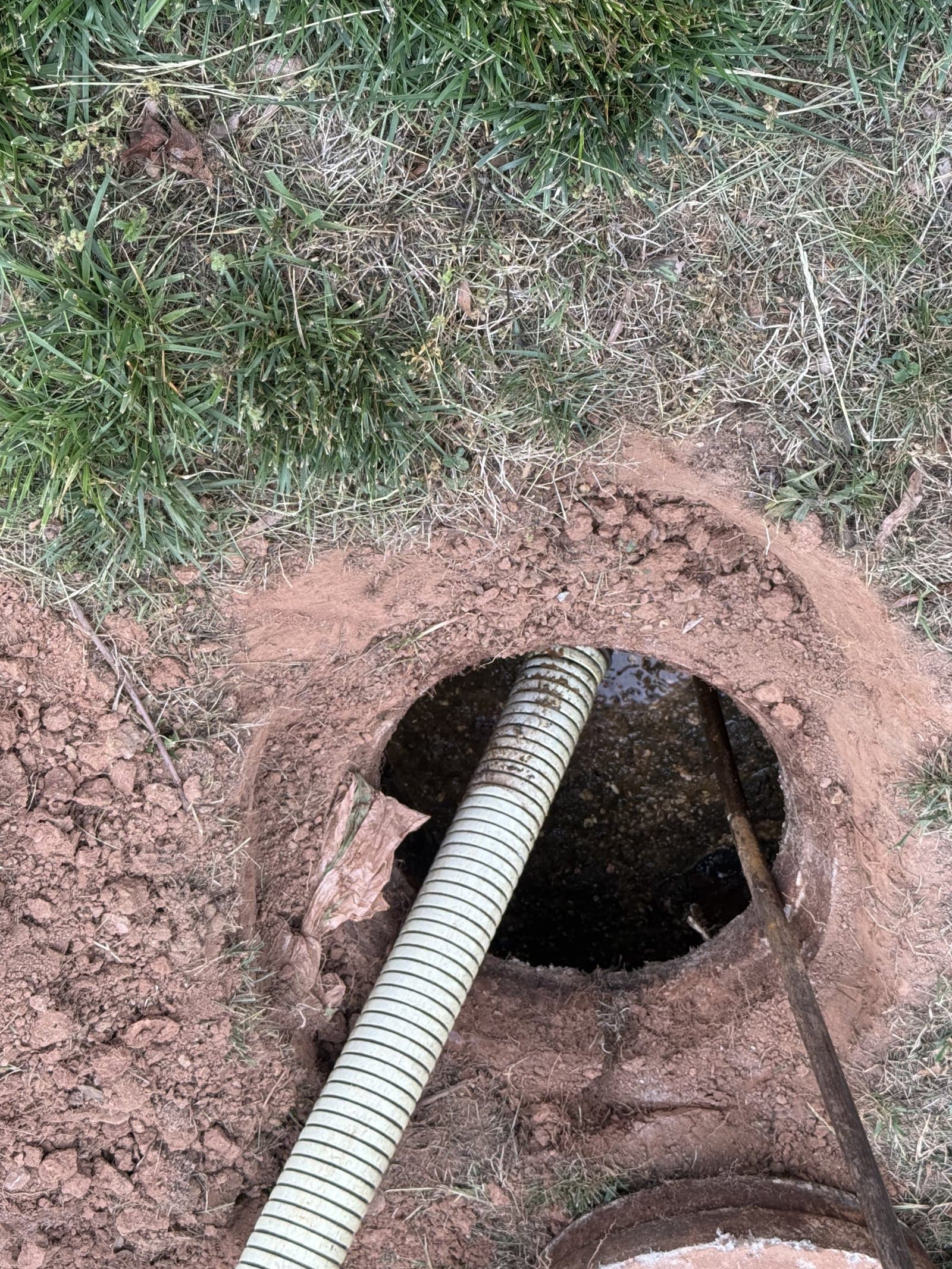 Overhead shot of the vacuum hose inserted into the open septic tank, mid-pump