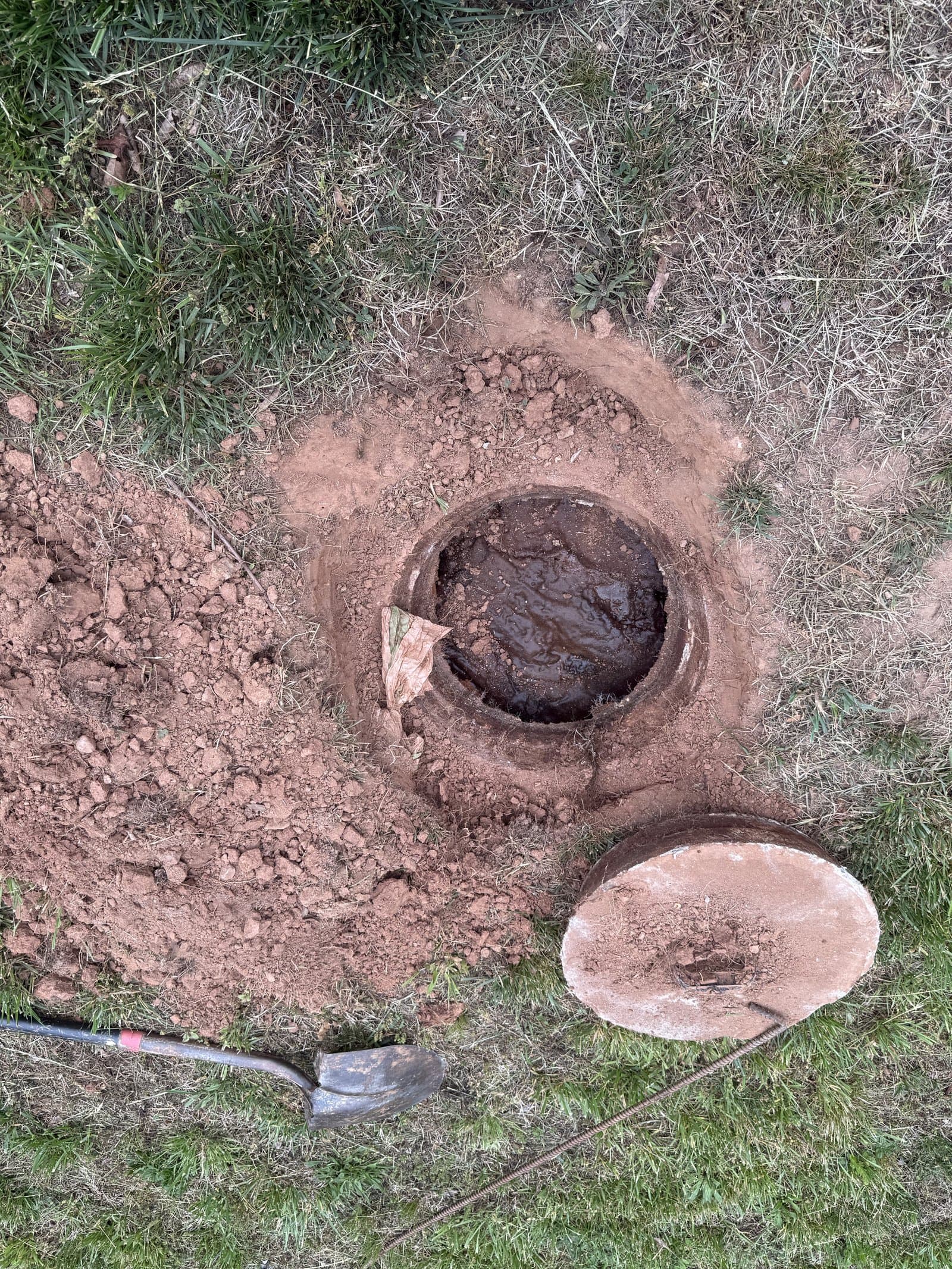 Overhead view of an excavated septic tank with the lid removed, ready for pumping